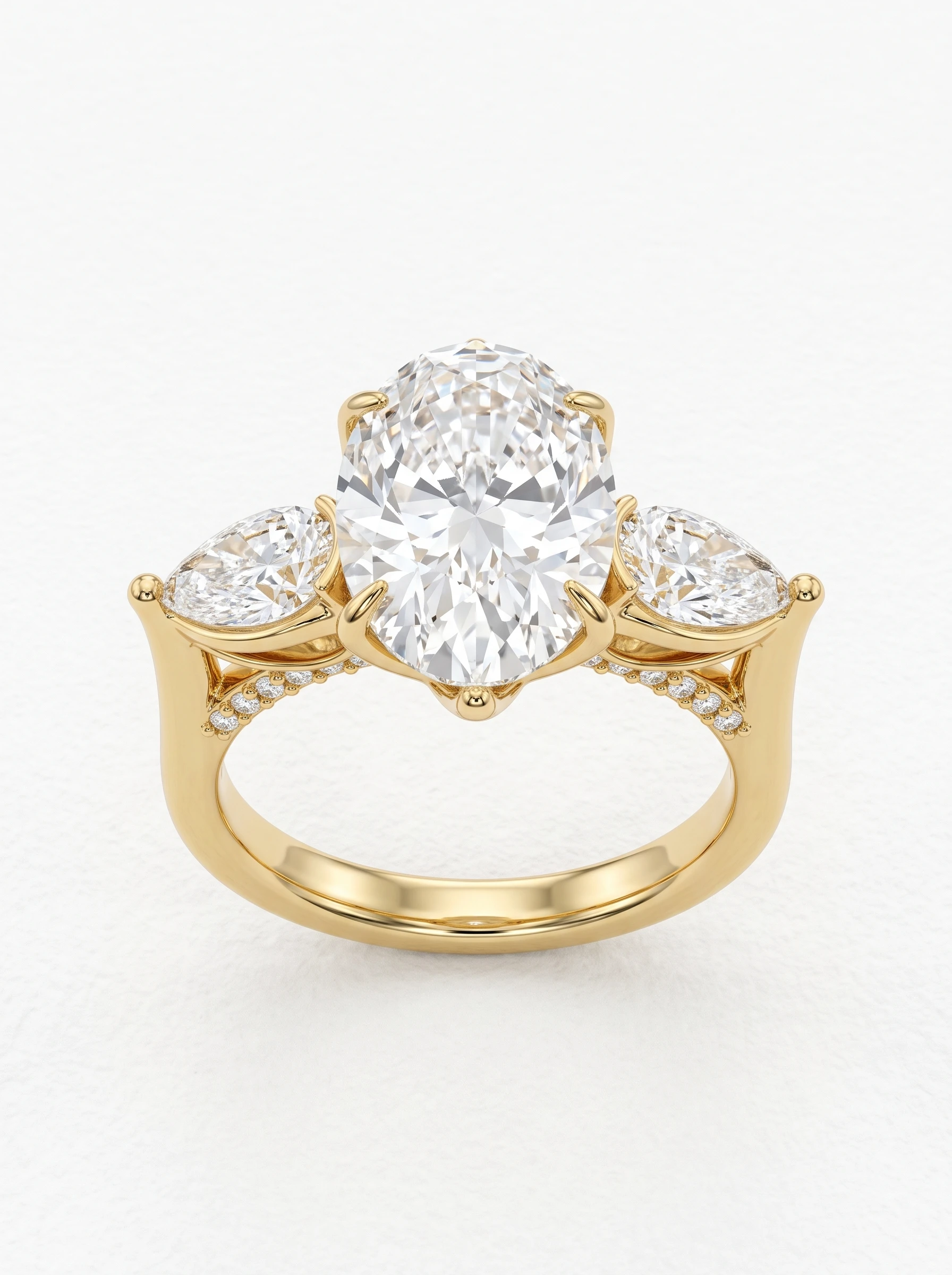 Oval and pear three stone engagement ring in yellow gold, front view with six claw prongs and pavé bridge