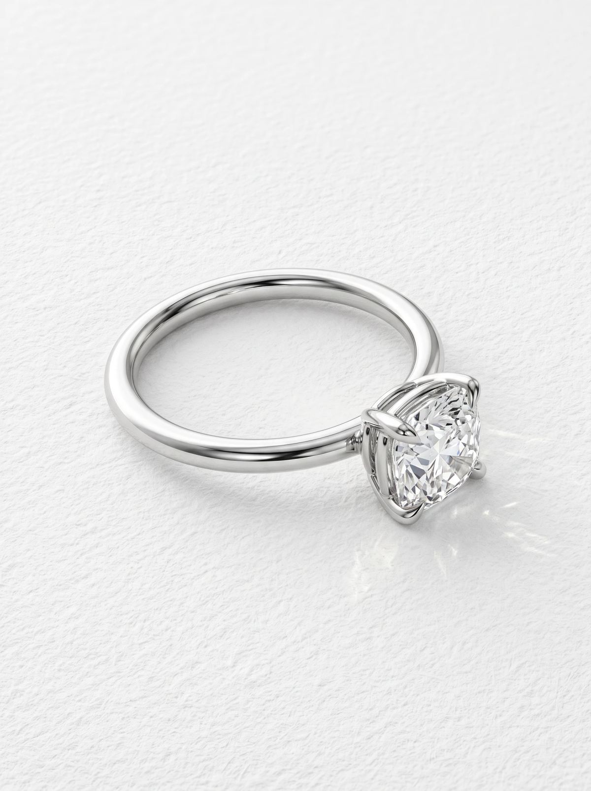 Bague de fiançailles coussin en platine couchée sur le côté, montrant le serti panier surélevé et l'anneau poli