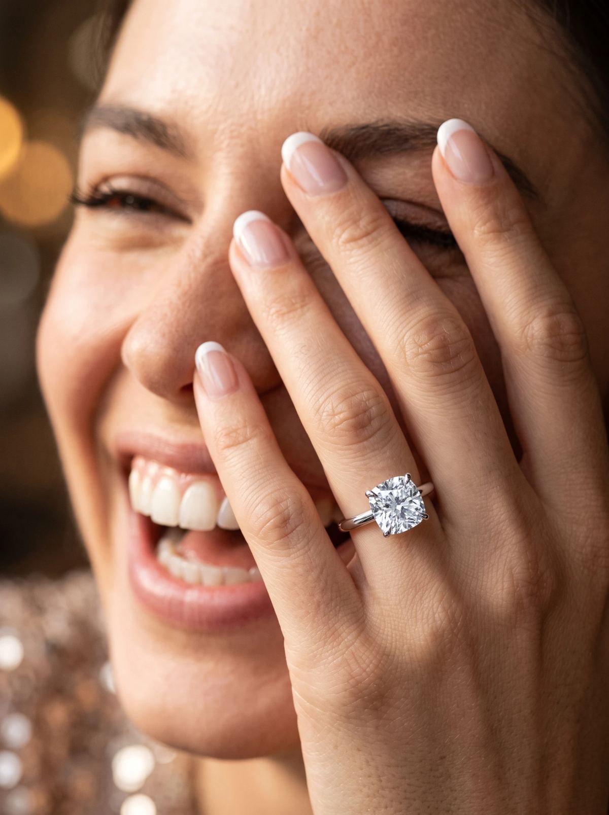 Solitaire coussin en platine porté à l'annulaire d'une femme qui rit, la main levée devant le visage
