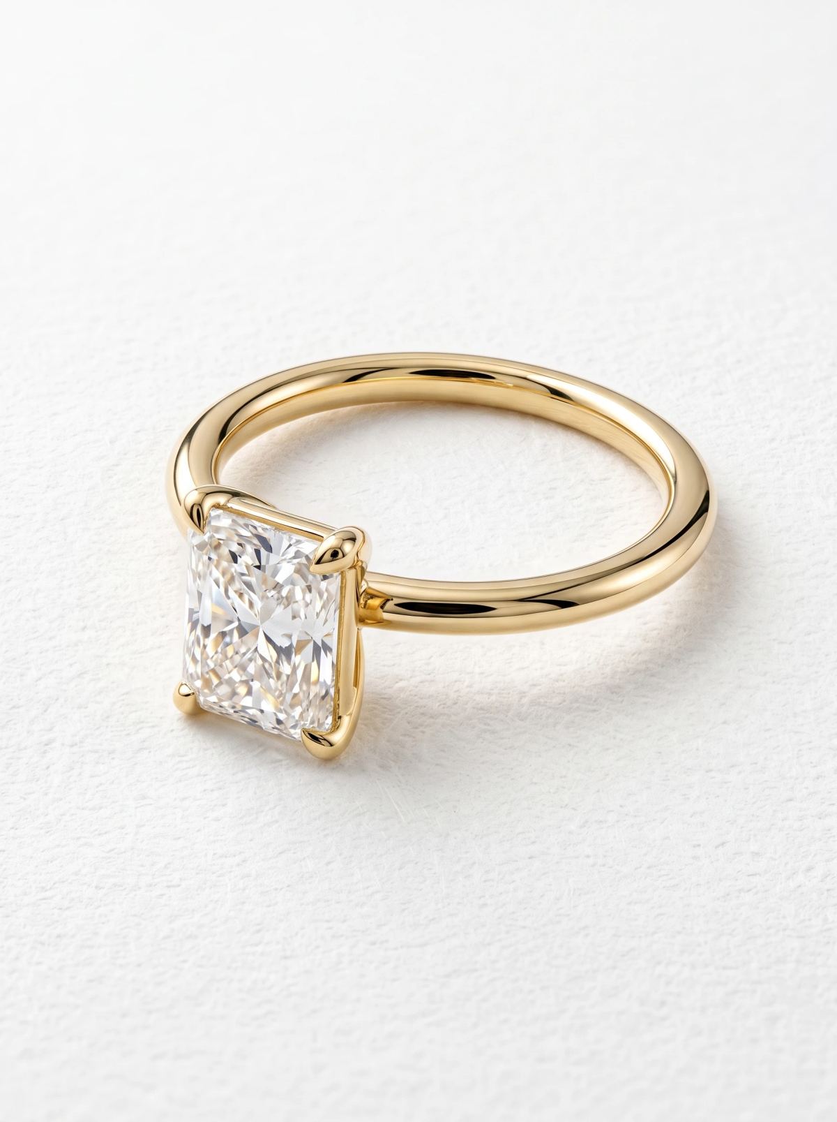 Bague de fiançailles radiant en or jaune posée à plat, pierre allongée au-dessus d'un anneau fin poli