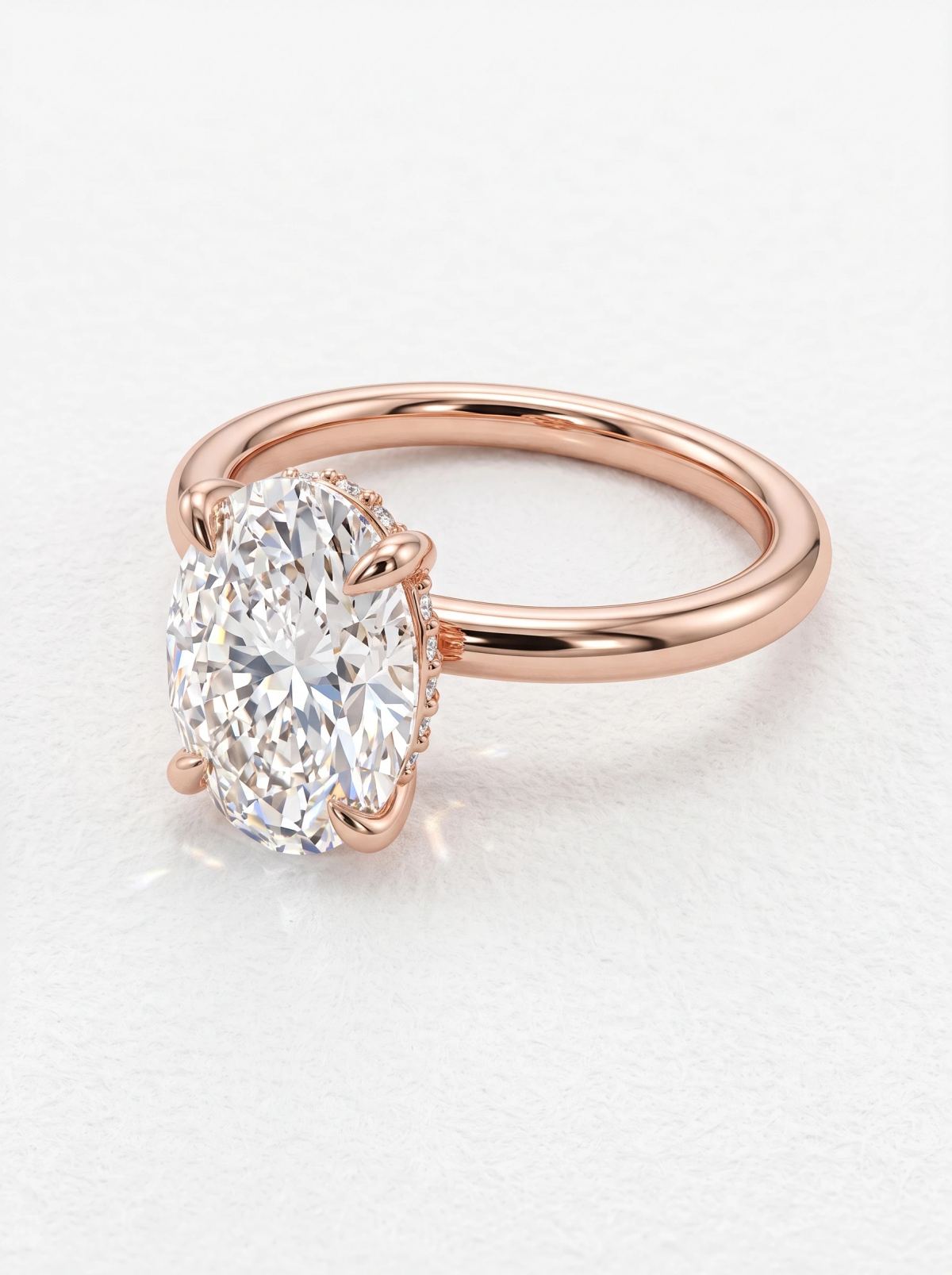 Vue rapprochée de dessus d'une bague ovale à quatre griffes en or rose, halo caché visible sur le côté