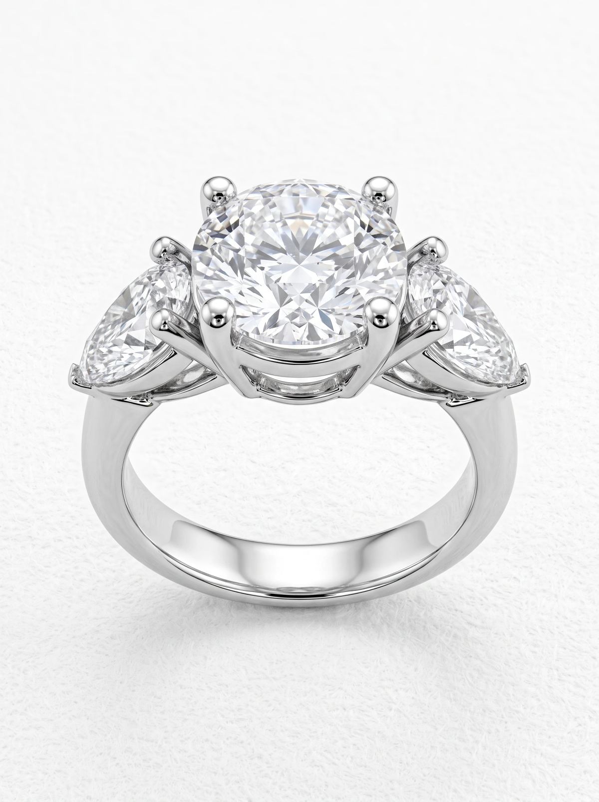 Vue de face d'une bague trilogie en platine, pierre ronde tenue par quatre griffes entre deux poires