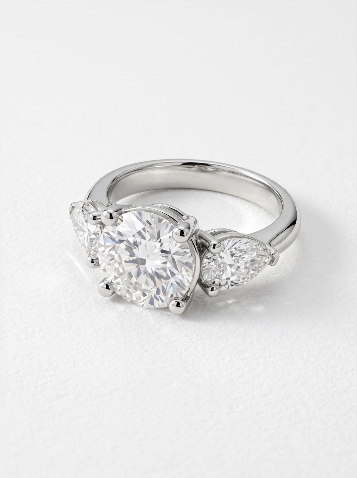 Bague trilogie en platine couchée sur le côté, pierre ronde et poire latérale sur anneau poli