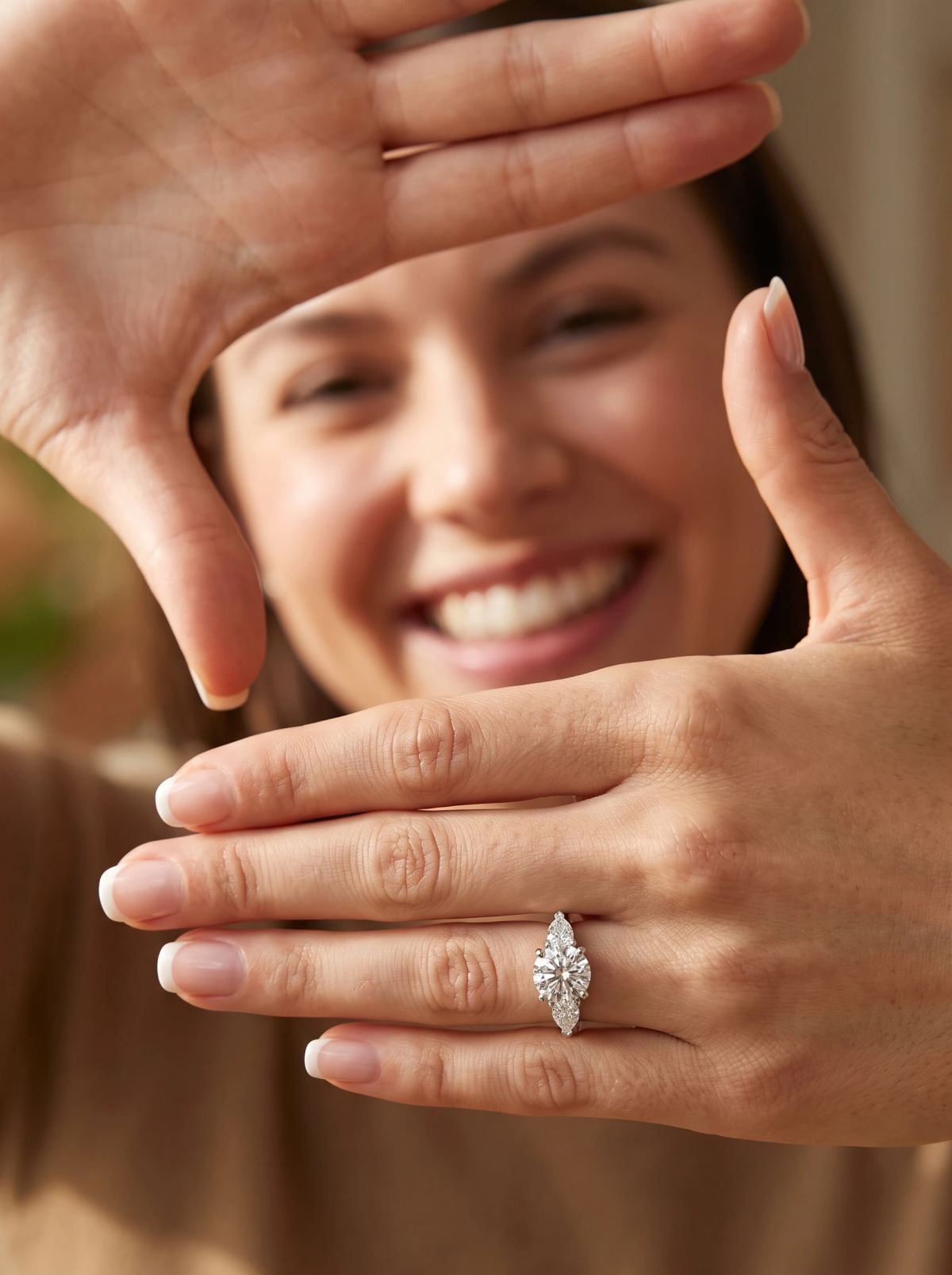 Bague trilogie ronde et poires portée à la main, des mains encadrant un visage souriant