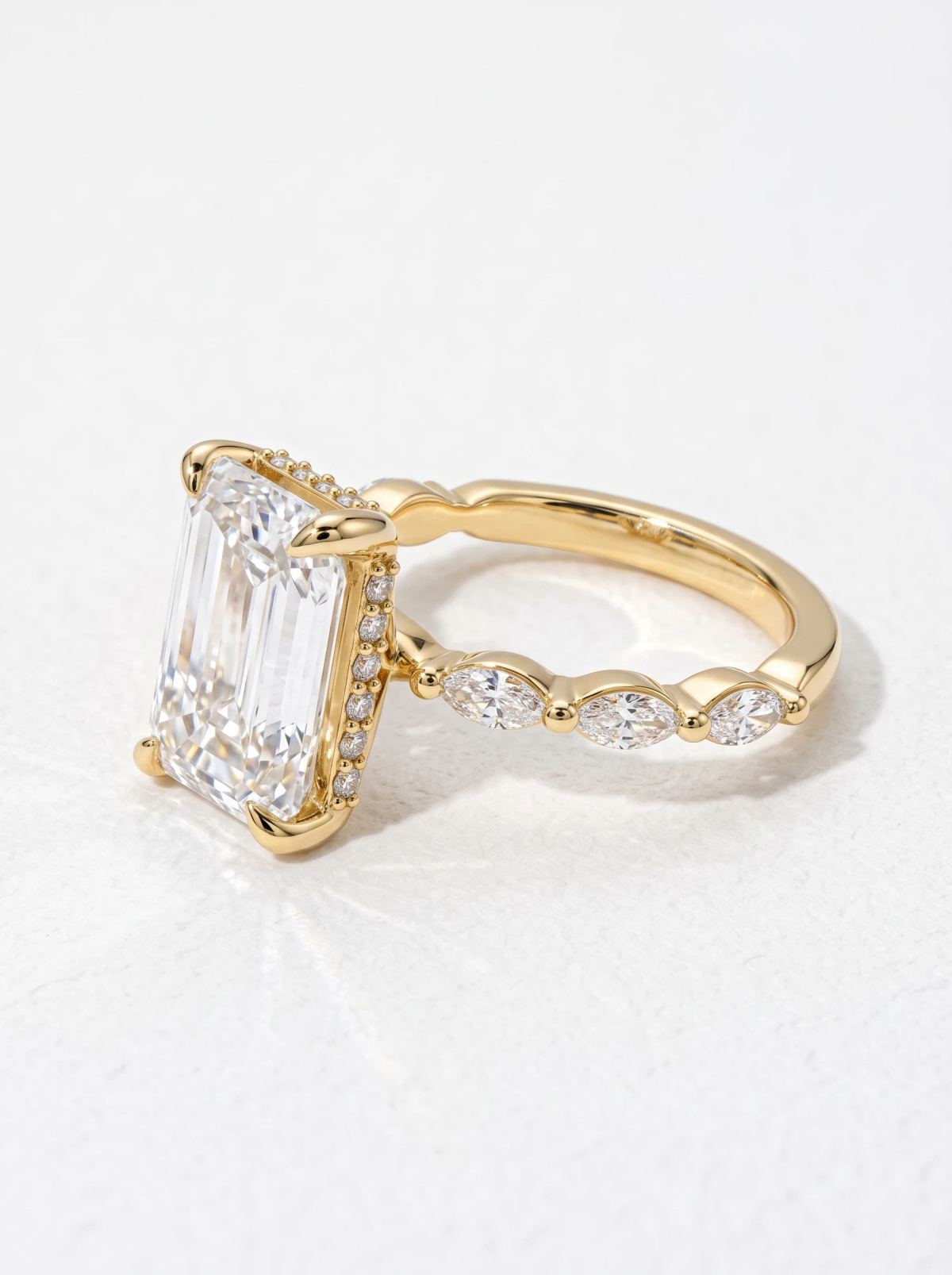 Vue de côté d'une bague taille émeraude en or jaune, halo caché pavé et trois marquises sur l'anneau