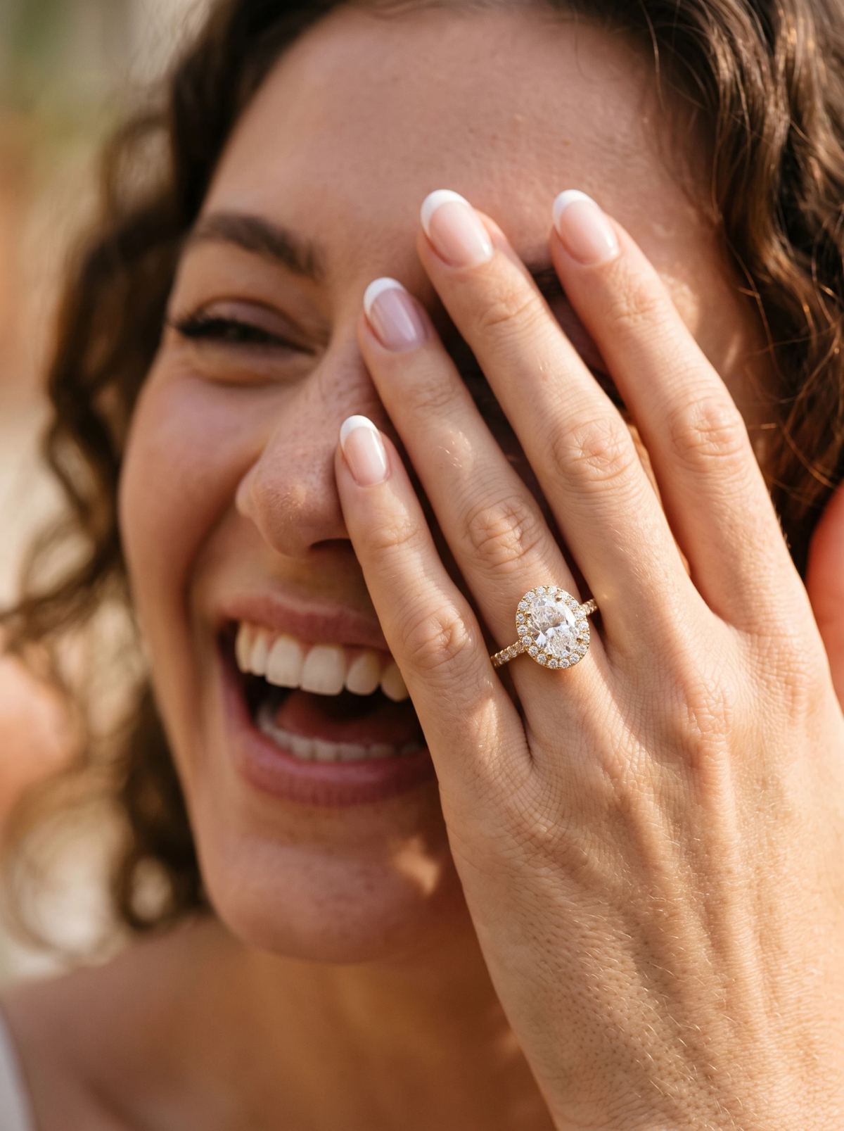 Bague halo ovale portée à la main, main levée près du visage d'une mannequin souriante