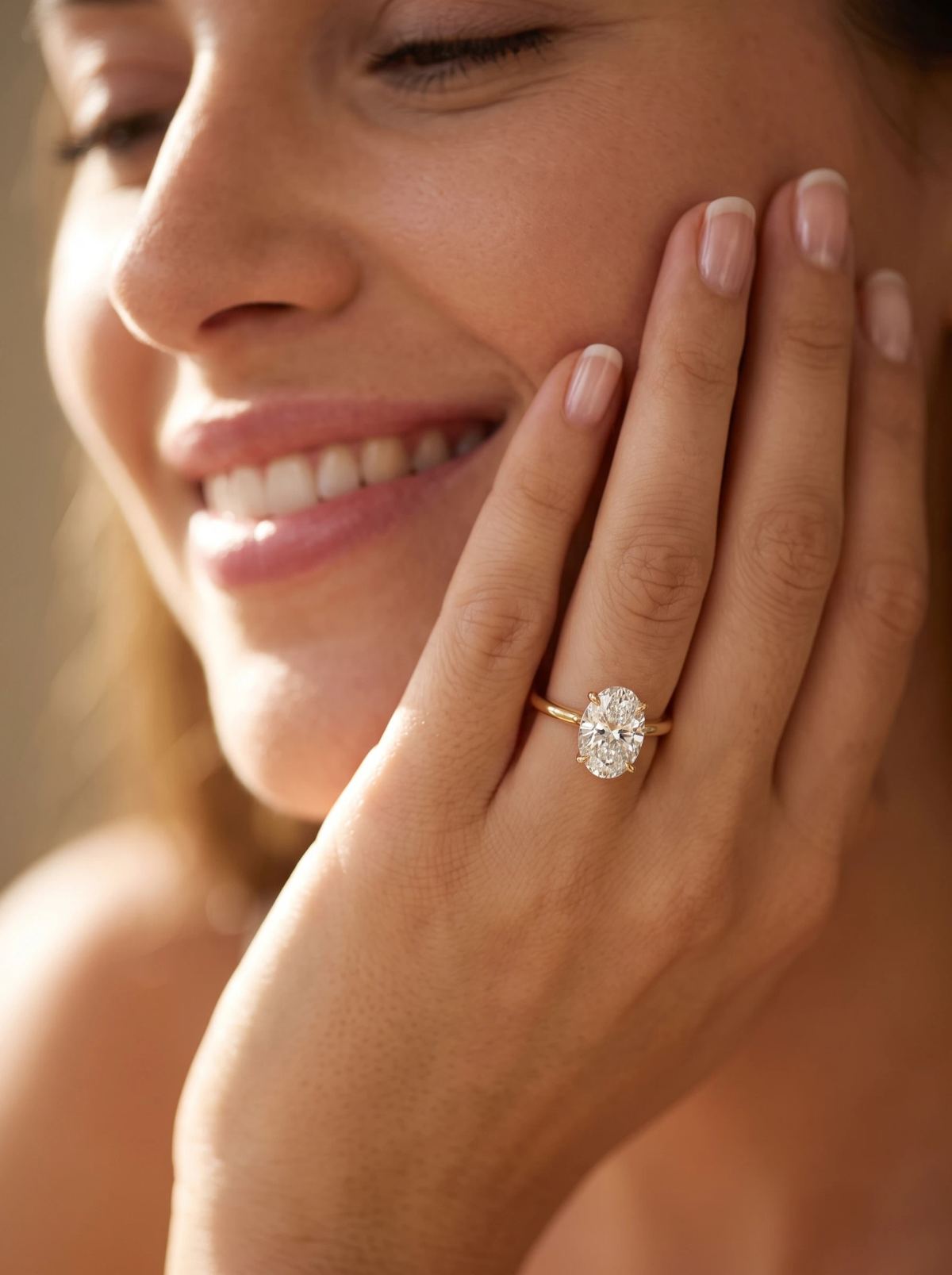Solitaire ovale en or jaune porté à la main, posée contre la joue d'une femme souriante
