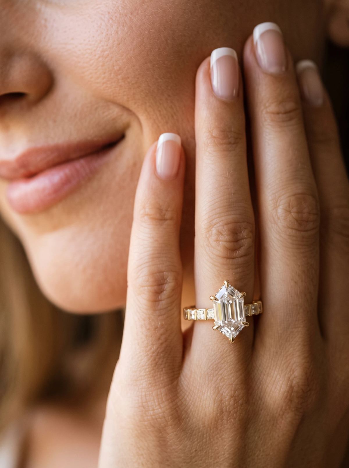 Bague de fiançailles hexagonale allongée en or jaune portée sur une main posée contre la joue