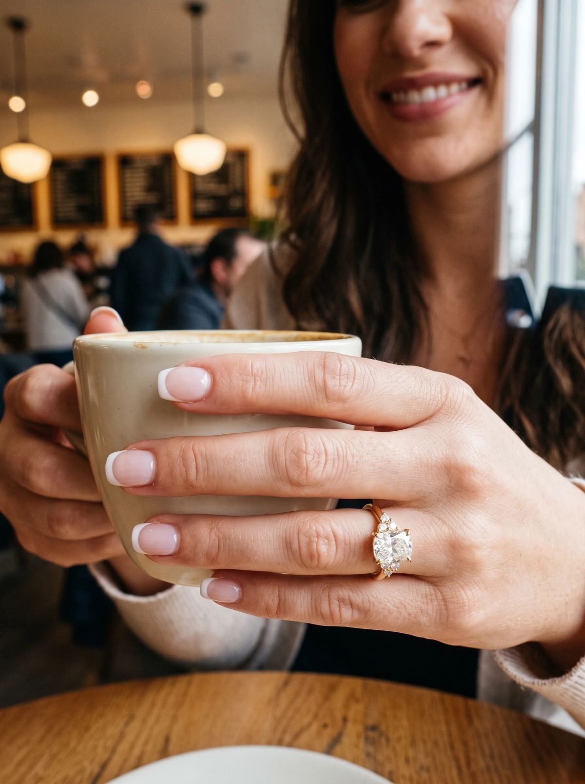 Bague de fiançailles coussin allongé en or jaune portée à la main autour d'une tasse de café