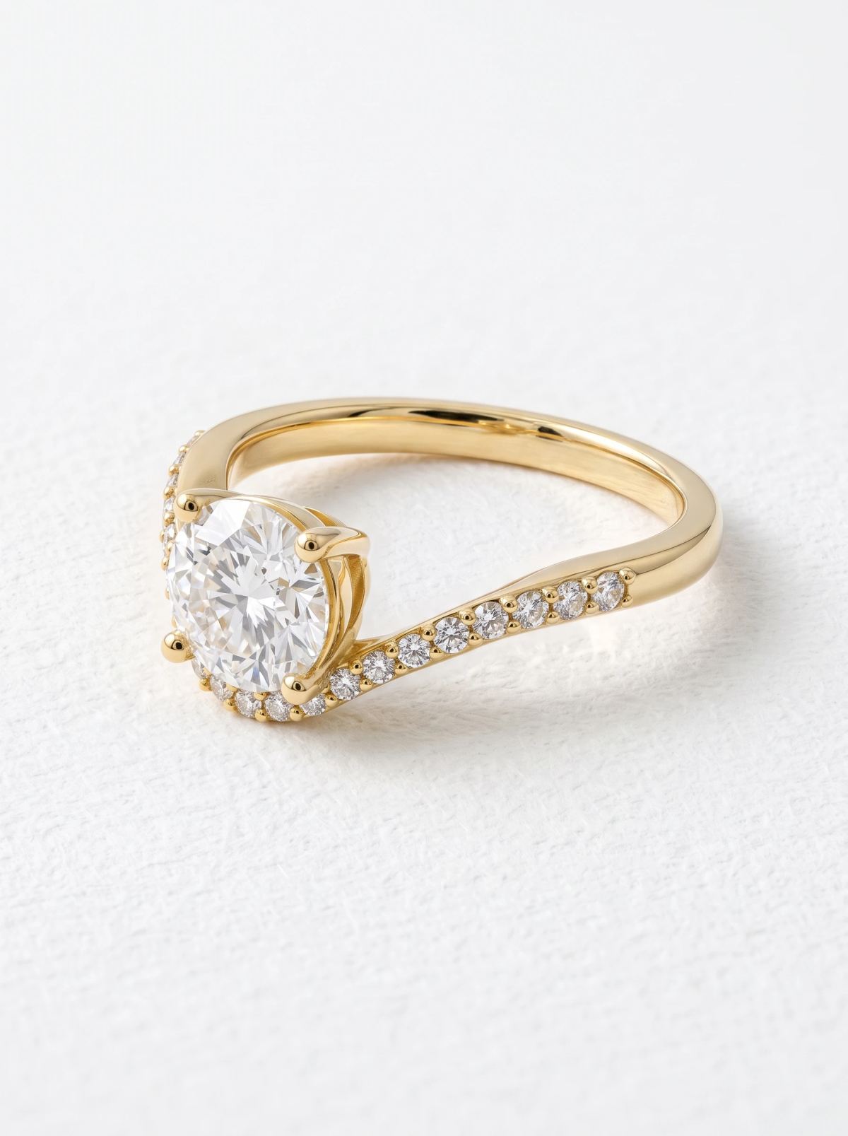 Bague en or jaune avec diamant rond vue en angle, bras pavé montant vers la pierre à quatre griffes