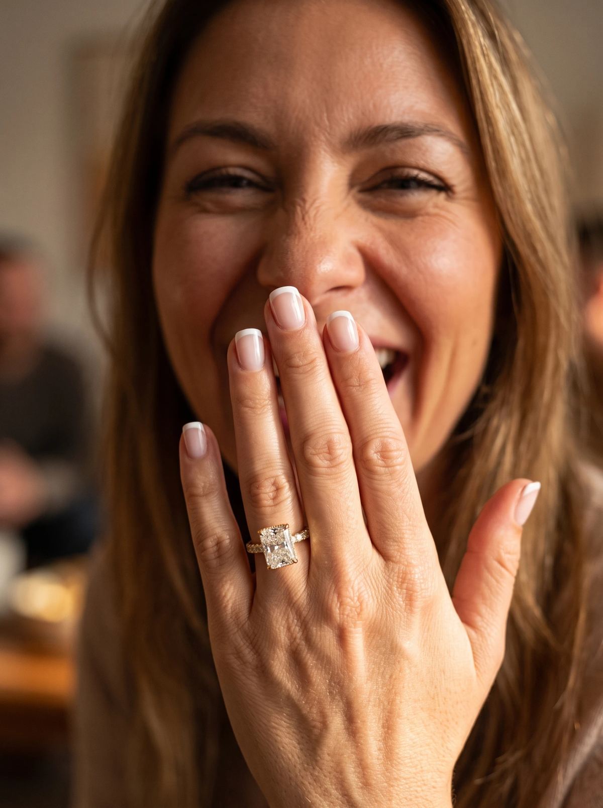 Bague de fiançailles radiant en or jaune portée sur une main levée devant la bouche d'une femme qui rit