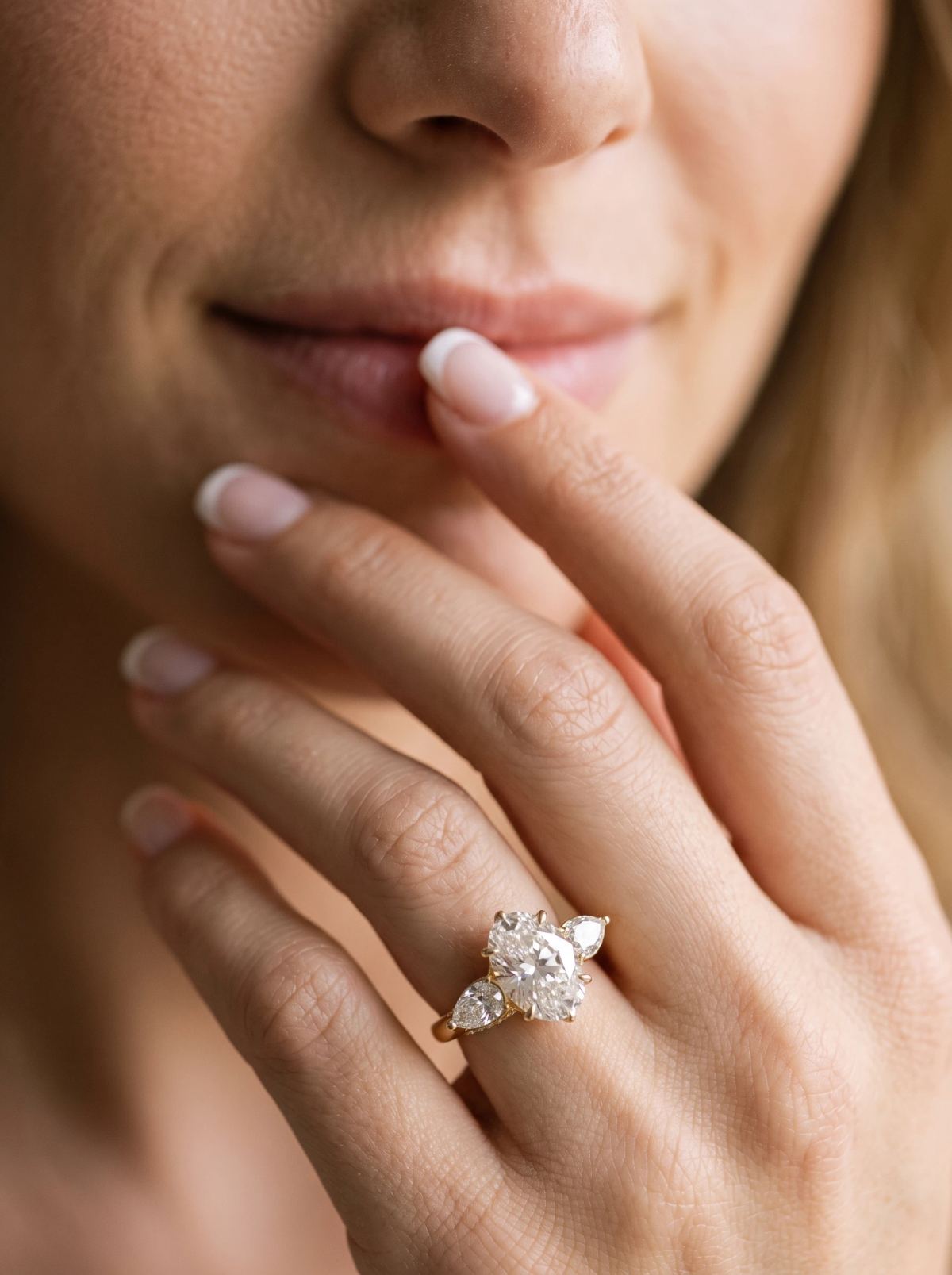 Bague trilogie ovale en or jaune portée à la main, le bout des doigts posé sur les lèvres