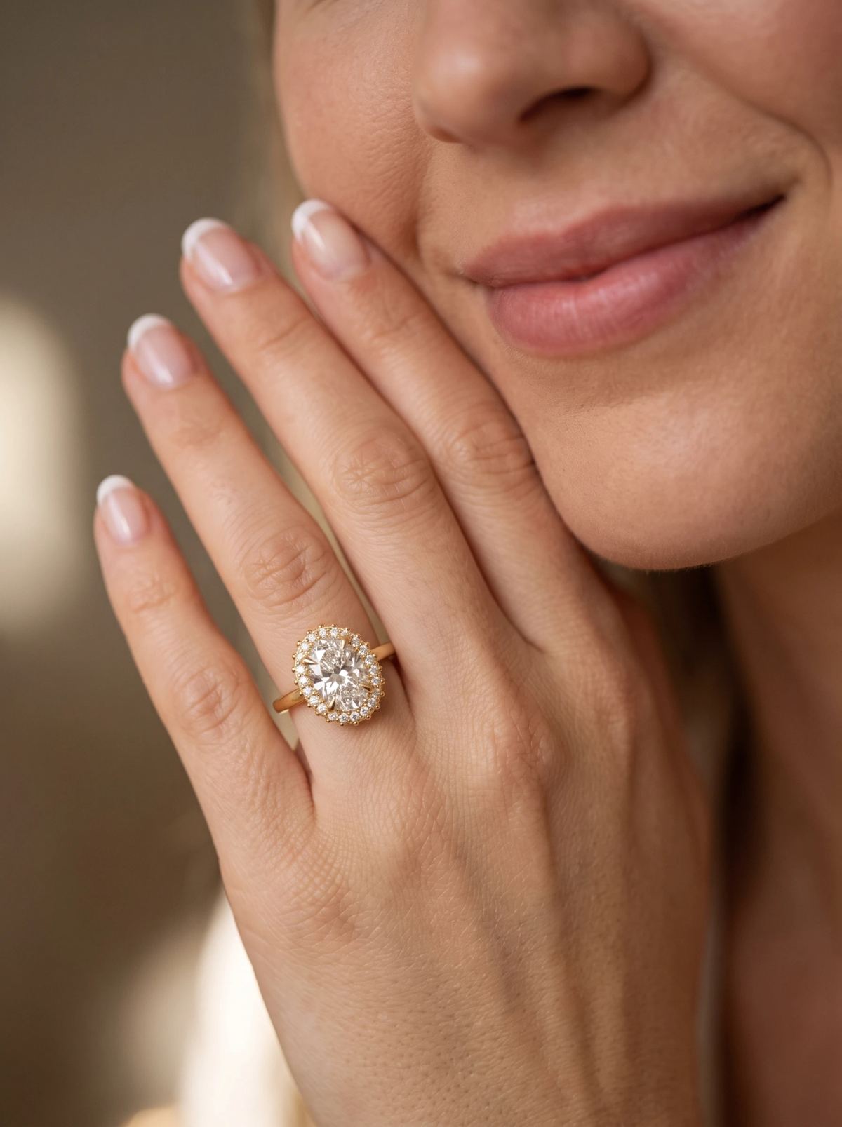 Bague de fiançailles ovale à halo en or jaune portée sur une main posée contre la joue