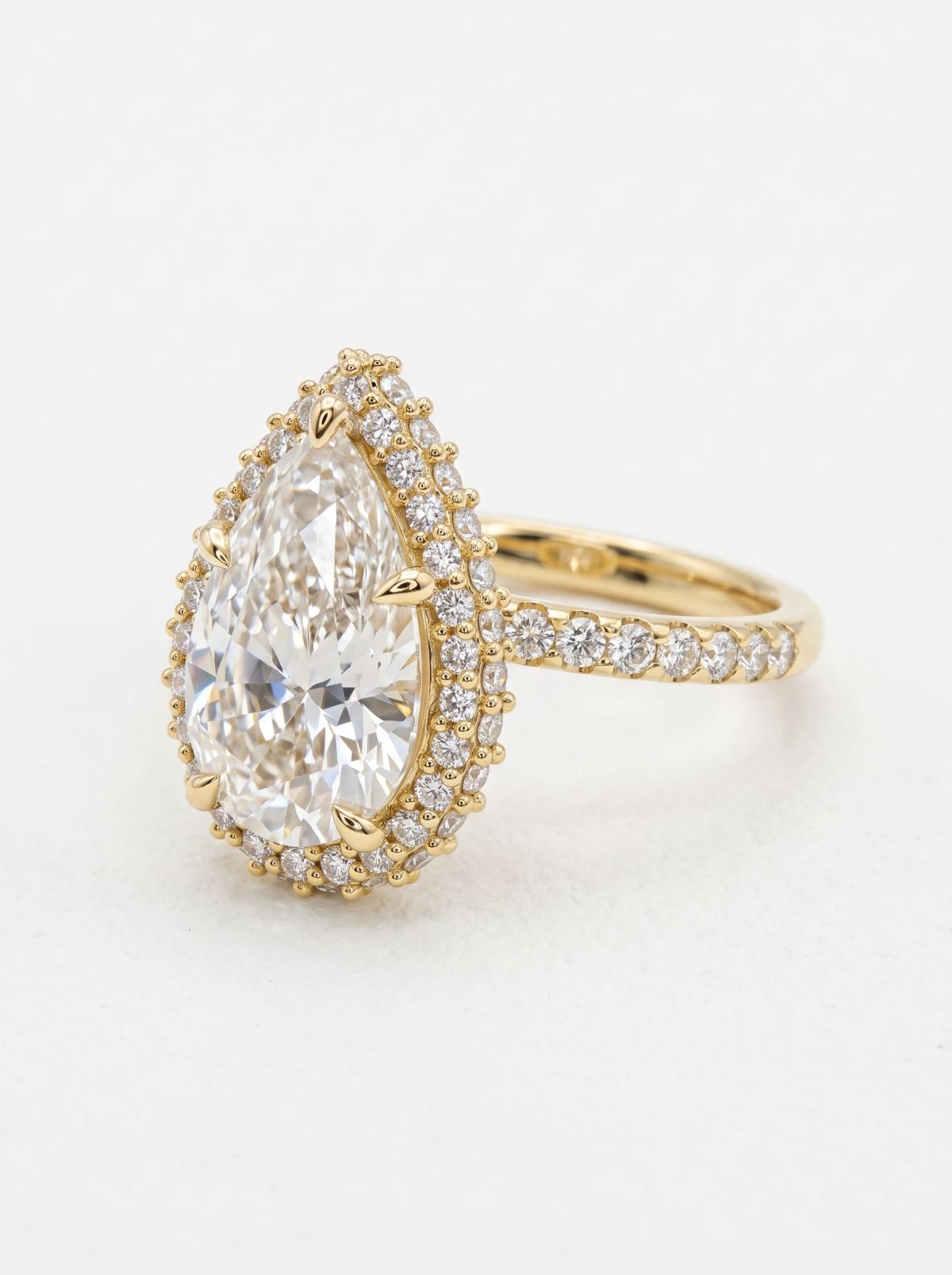 Vue trois quarts d'une bague de fiançailles poire en or jaune, double halo et anneau serti pavé